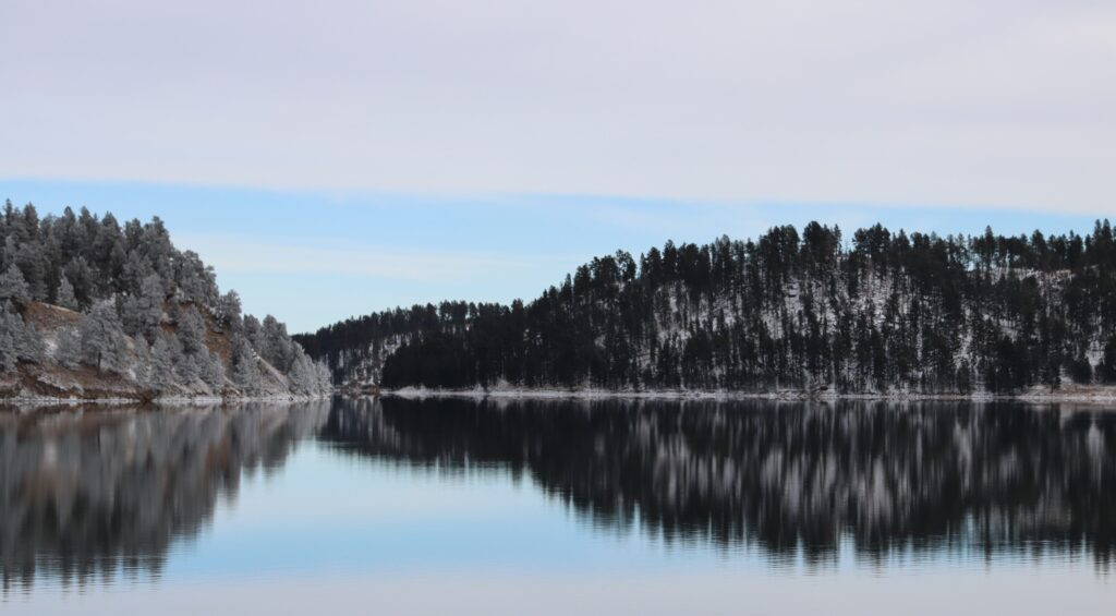 Reflections Of A Winter Wonderland: The Black Hills 4 mirror-flat deerfield lake in spearfish canyon reflecting snow-covered evergreens and an overcast winter sky.