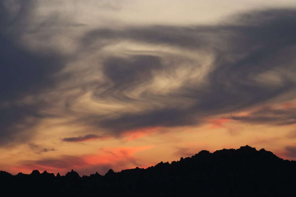 Photography Tours In The Badlands 1 jagged badlands ridge silhouetted against swirling charcoal, gray, and amber sunset clouds in badlands national park